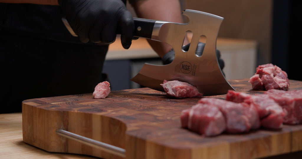 A man's hand with gloves chopping meat using the Gladiator Series Meat Chopper 8" with Acacia Wood Stand