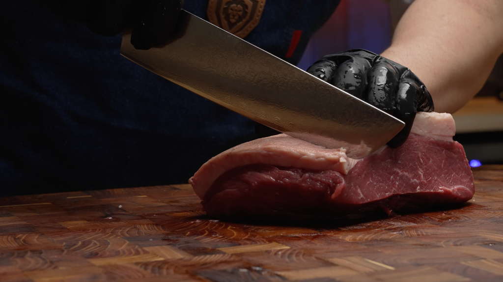 A man with black gloves slicing meat using the Shogun Series ELITE Tanto Chef's Knife 8"