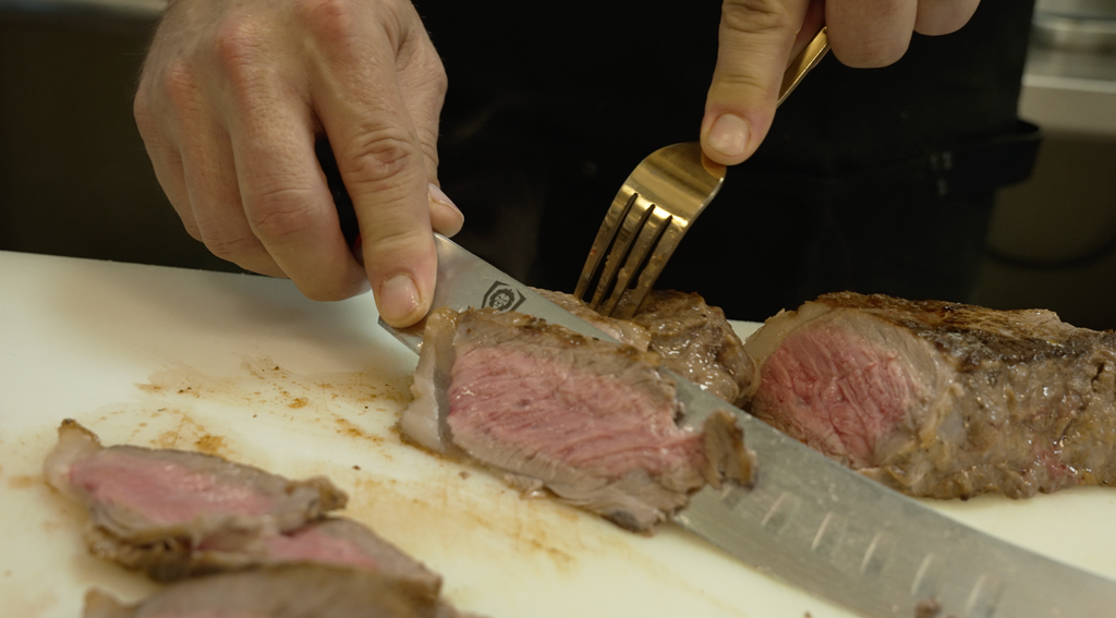 A man slicing a steak using the Shogun Series ELITE Butcher's Breaking Cimitar Knife 10"