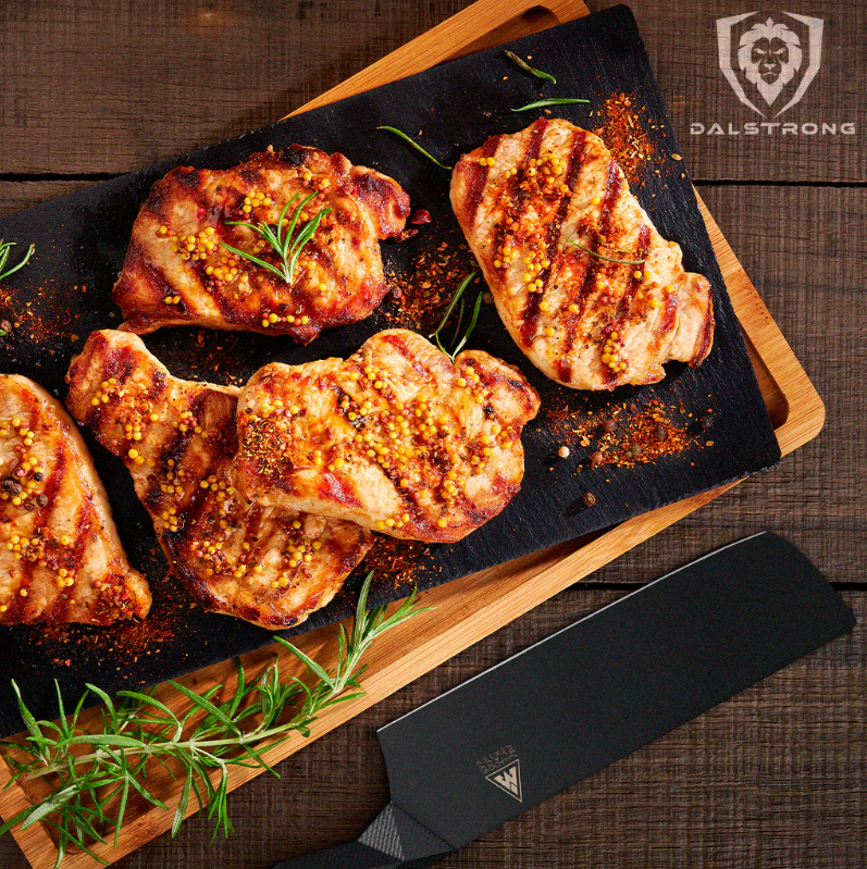 Delicious boneless Pork Chops on a black platter with wooden cutting board underneath and the Shadow Black Series Nakirion the side on the side.