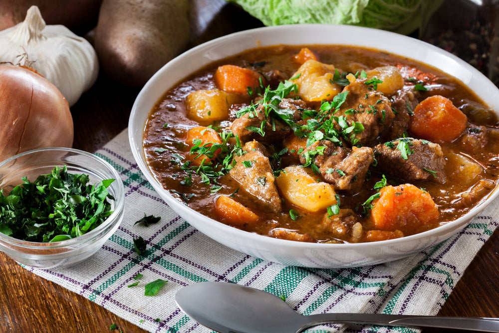 Traditional Irish beef stew in a white bowl on a checkered kitchen towel on a wooden towel