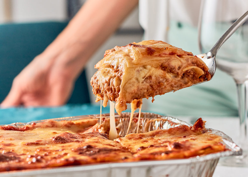 Woman serving portion of lasagna food from a foil baking tray